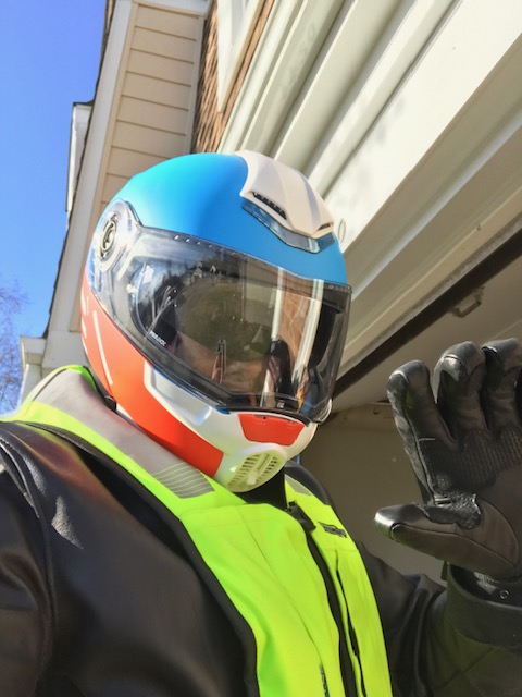 Motorcycle rider wearing helmet, leather jacket, gloves, and Helite airbag vest.