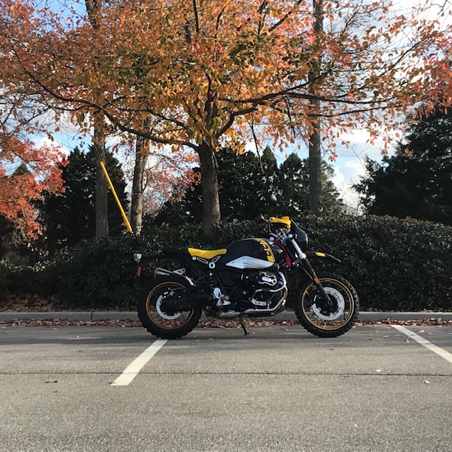 BMW R Nine T Urban GS yellow and black motorcycle under yellow-leafed tree in parking lot.