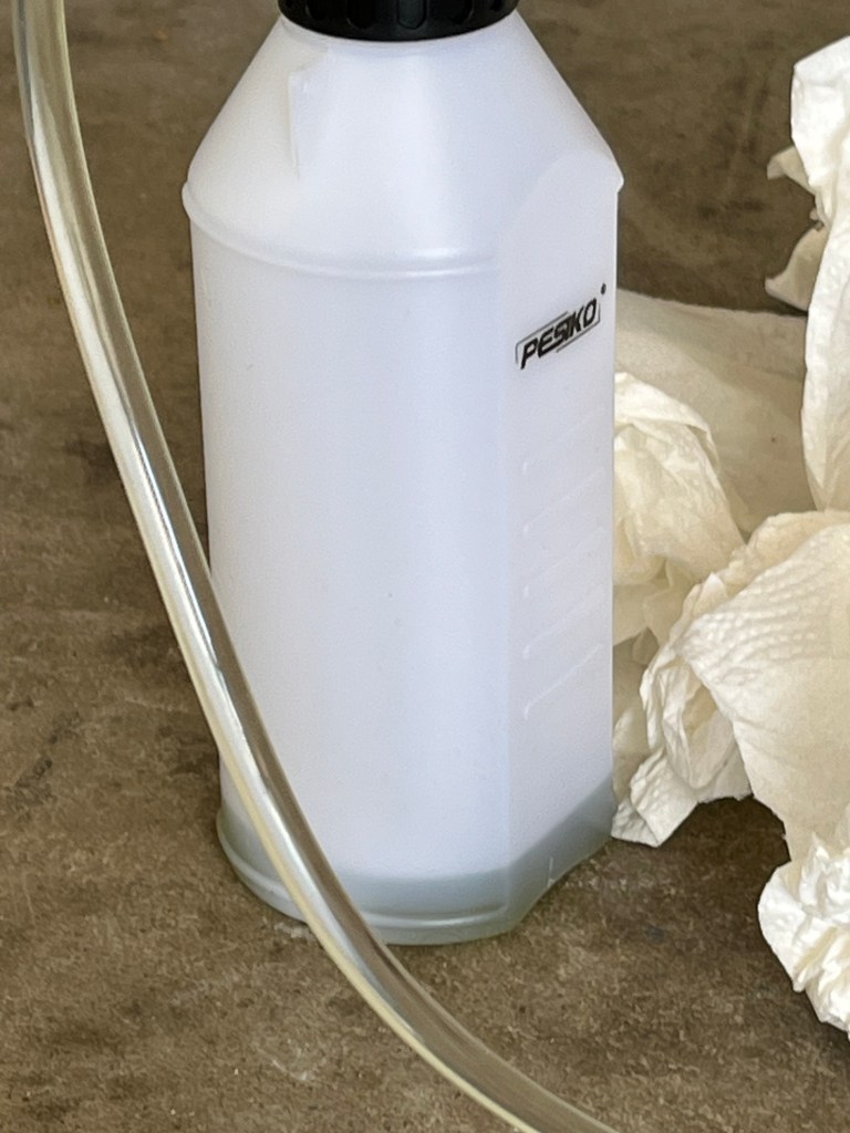 plastic bottle with hose and dark liquid at the bottom with crumpled paper towels to the right