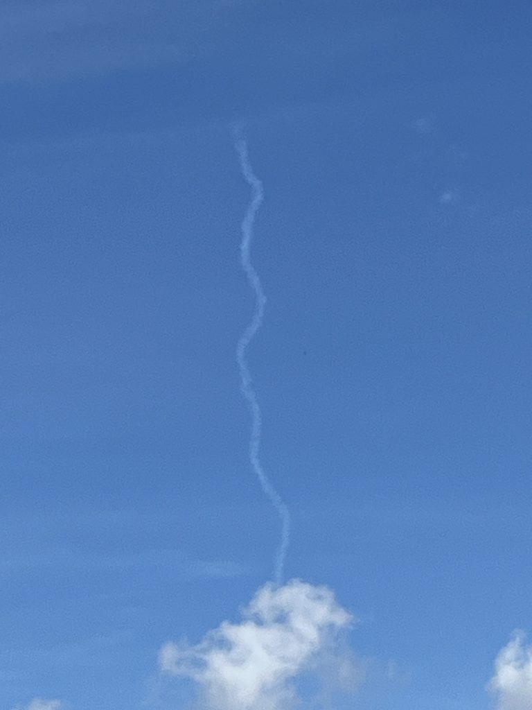 blue sky with jet contrail rising up from wispy cloud
